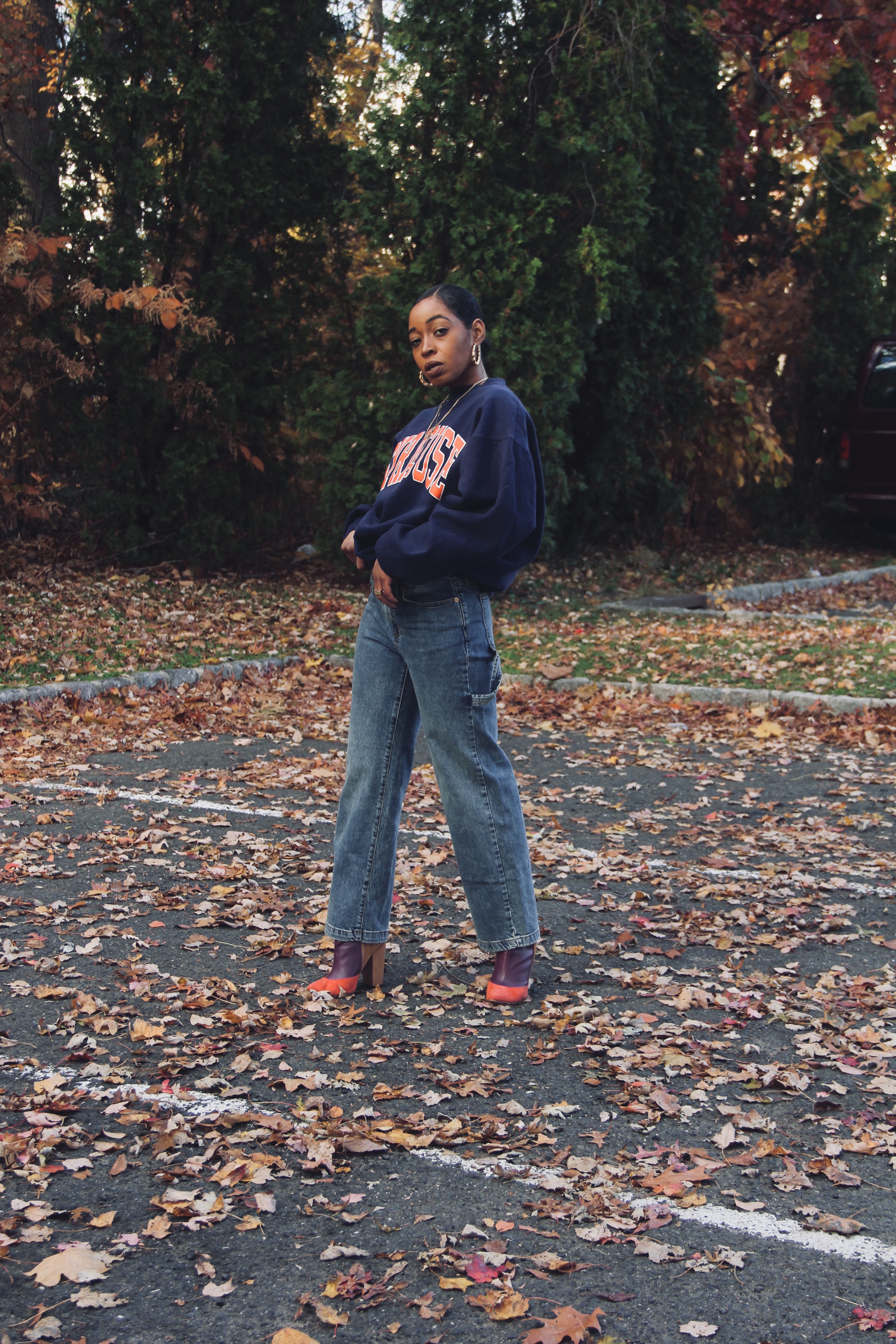 STACi P wearing a Syracuse vintage college sweatshirt with a MCM belt bag and color block ankle boots in a setting of colorful Fall leaves. 